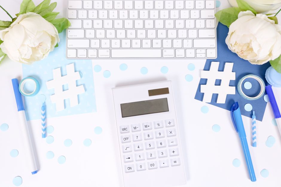 Styled stock photo with a calculator, white flowers, and blue office supplies on a desk.
